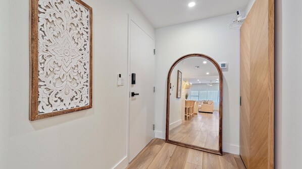 Un couloir doté d’un plancher en bois, d’une porte blanche et d’un panneau décoratif sur le mur.