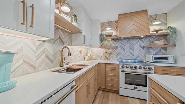 A modern kitchen with a herringbone tile backsplash, a stainless steel range, and a built-in oven.