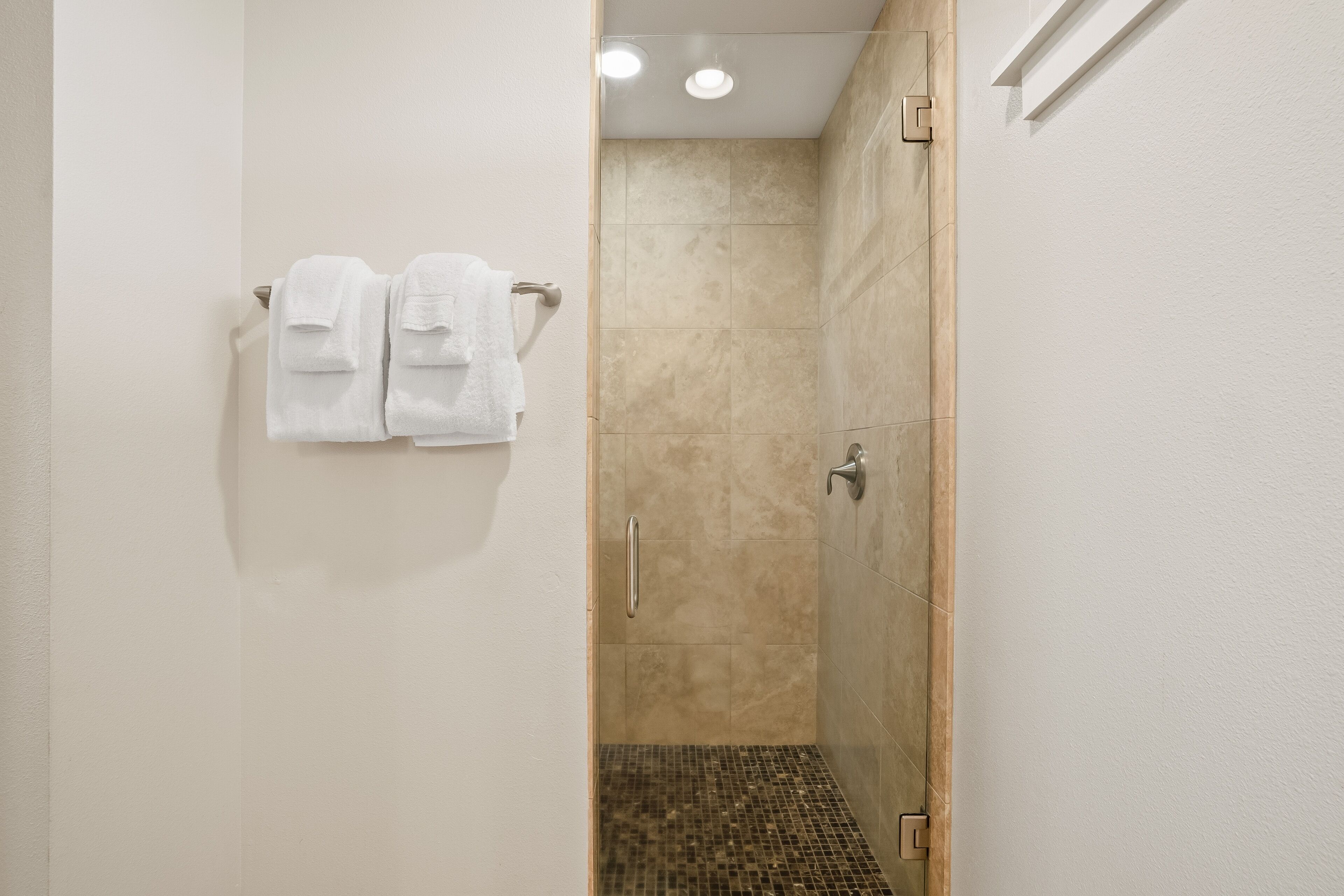 A bathroom with a shower, tiled walls, and a towel rack with two towels.