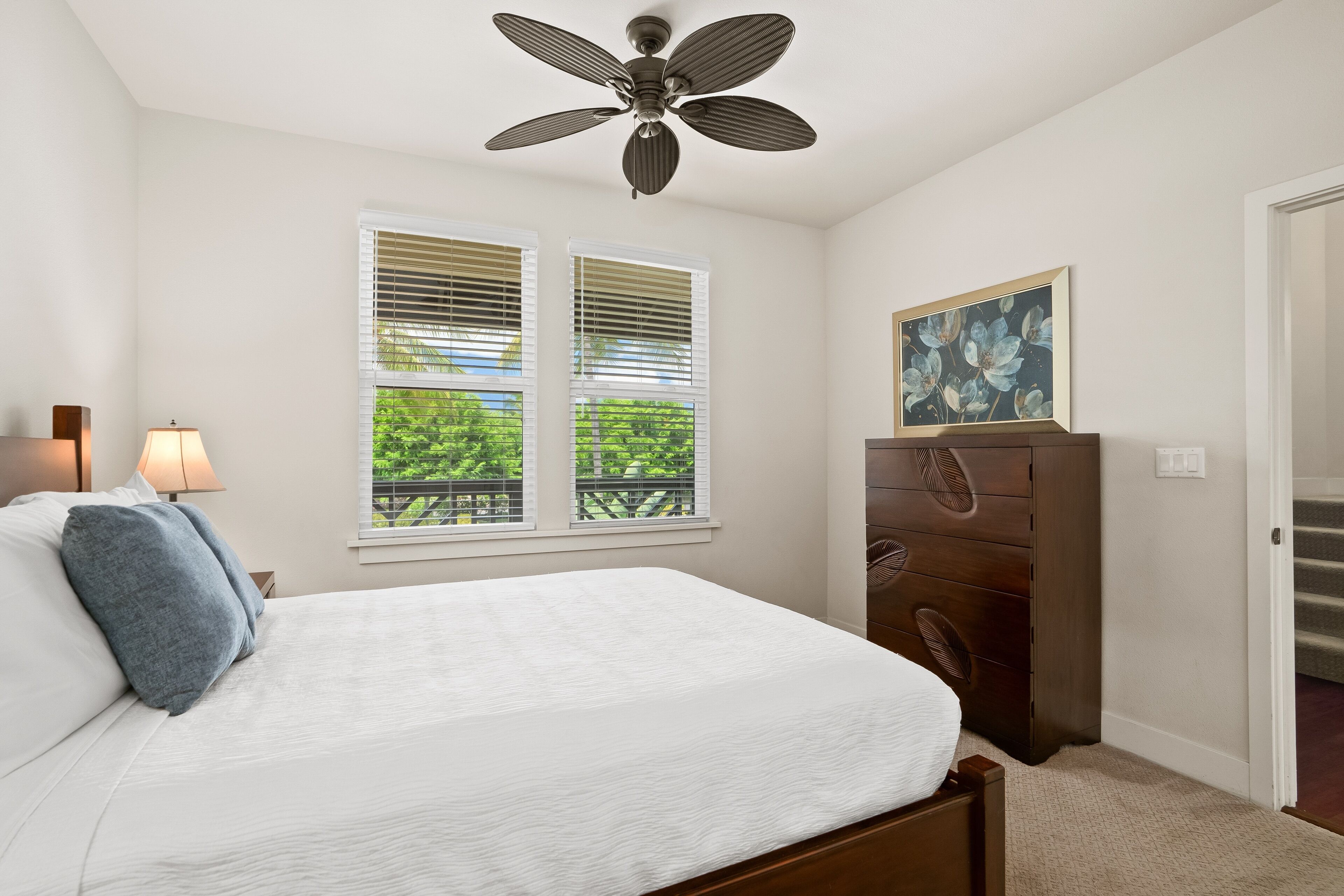 A bedroom with a bed, a ceiling fan, a dresser, and a window with blinds.