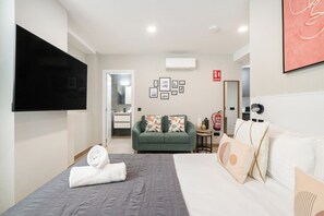 A modern hotel room with a large bed, a flat-screen TV, a green sofa, and a small side table. - Dobo Madrid Cabrera (Madrid)