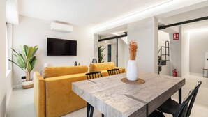 A modern living room with a wooden dining table, yellow sofa, and a mounted TV. - Dobo Madrid Cabrera (Madrid)