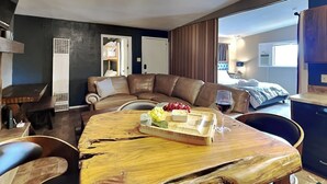 Un salón moderno con una mesa de comedor de madera, sofá de cuero y cama con una manta azul.