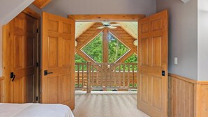 A bedroom with a large wooden door leading to a balcony with a wooden railing and a view of trees.