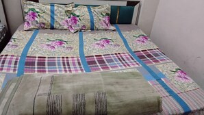 A bed with a floral and plaid bedspread, a green blanket, and a headboard with a teal accent.
