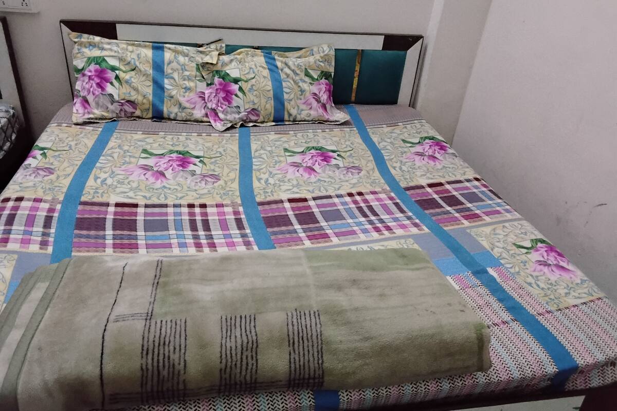 Un lit avec une couvre-lit à motifs floraux et à carreaux, une couverture verte et une tête de lit agrémentée d’une touche de couleur turquoise.
