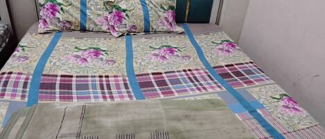 A bed with a floral and plaid bedspread, a green blanket, and a headboard with a teal accent.