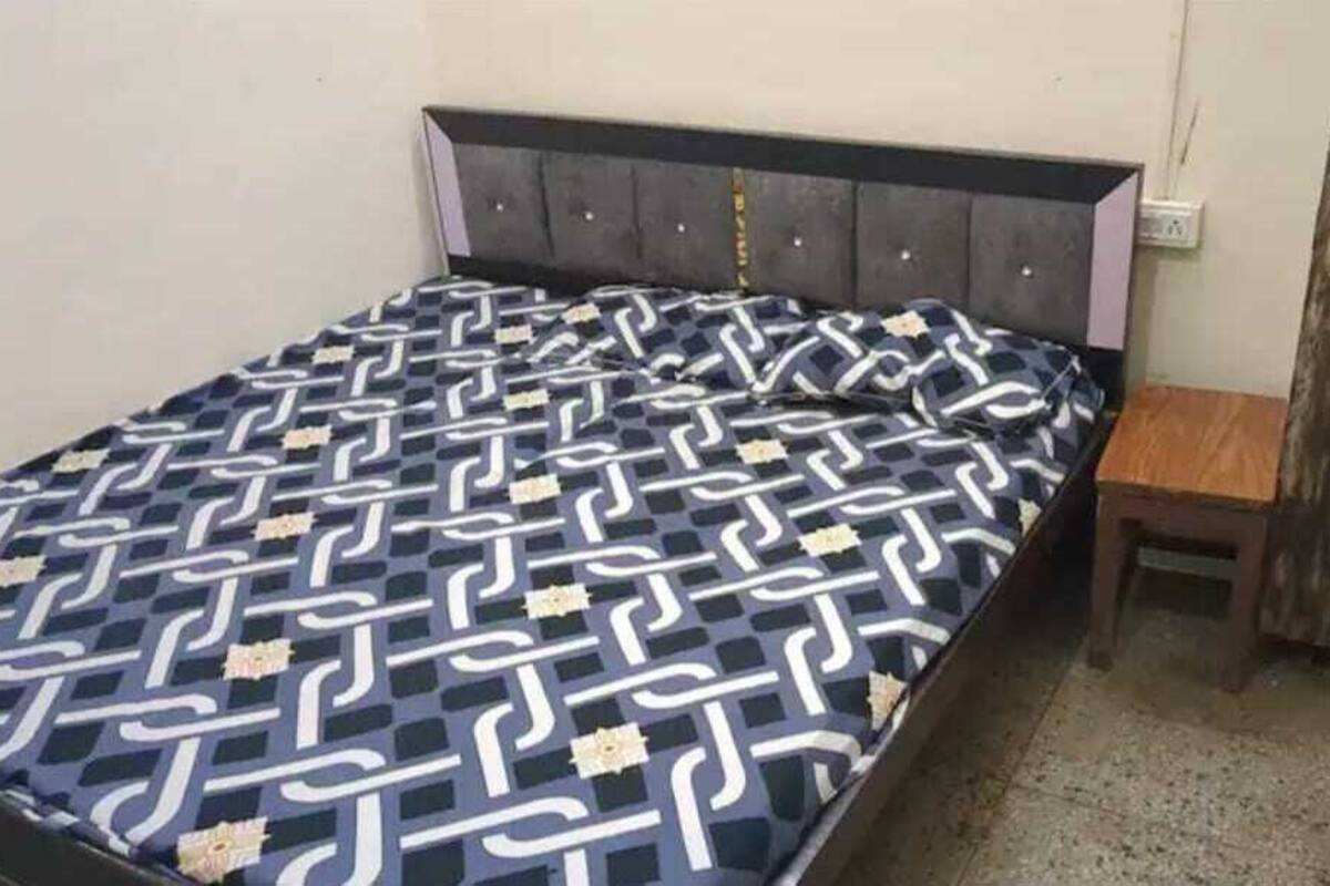 Un lit recouvert d’une couvre-lit à motifs, une table de chevet en bois et un panneau décoratif en bois fixé au mur.