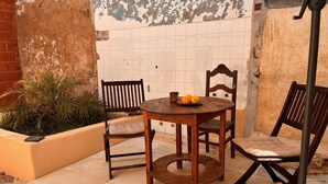 A wooden table with chairs and a small plant in a tiled outdoor area.
