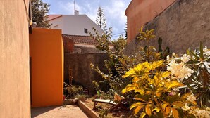 A narrow pathway leading to a building with a white facade and a red roof.