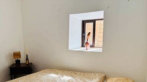 A bedroom with a bed, a nightstand, a lamp, and a window with a view of the outside.