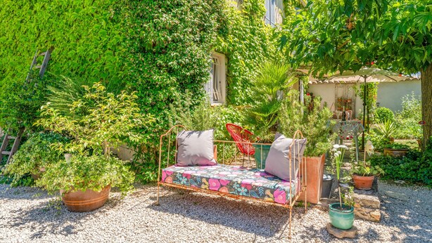 A garden with a metal bench, potted plants, and a building with ivy-covered walls. - Holiday Home 'Jardin' with Shared Pool, Private Terrace and Wi-Fi (L'Isle-sur-la-Sorgue)