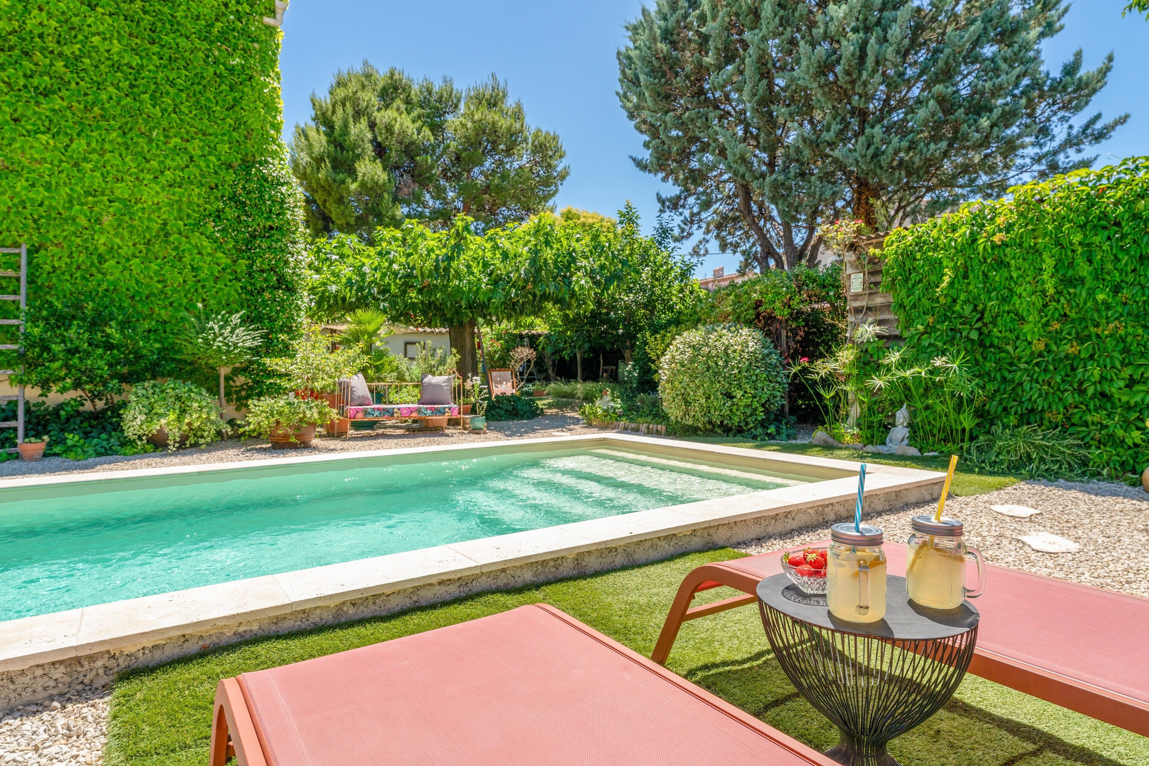 A swimming pool with a patio area, surrounded by lush greenery and trees.