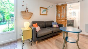 A living room with a sofa, a small table, a hanging basket, and a door leading to another room. - Holiday Home 'Jardin' with Shared Pool, Private Terrace and Wi-Fi (L'Isle-sur-la-Sorgue)