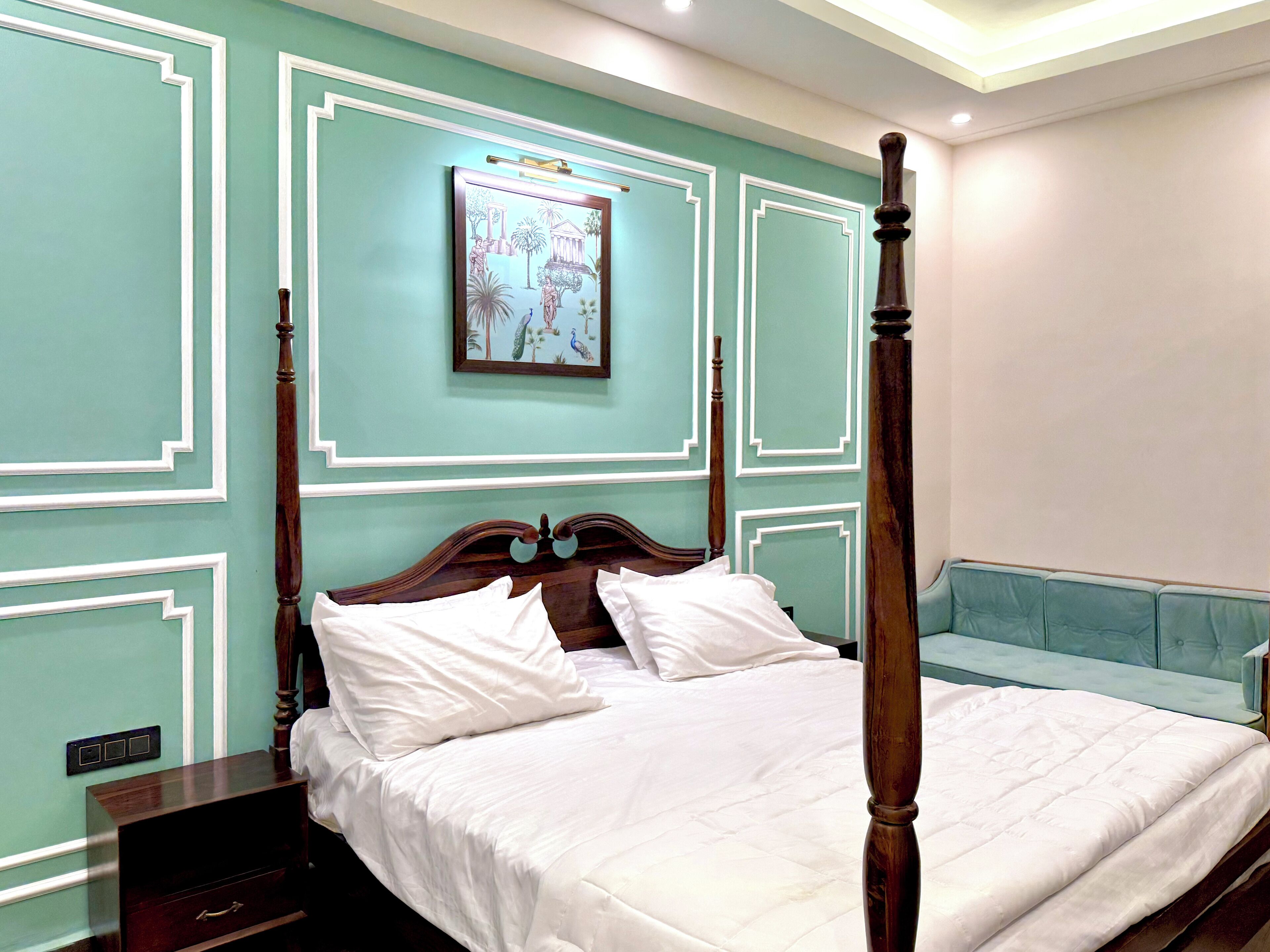 A four-poster bed with white linens, a nightstand with a drawer, and a wall-mounted picture.