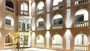 Un amplio patio con varios ventanales arqueados y balcones, una zona de recepción y una escultura decorativa de metal.