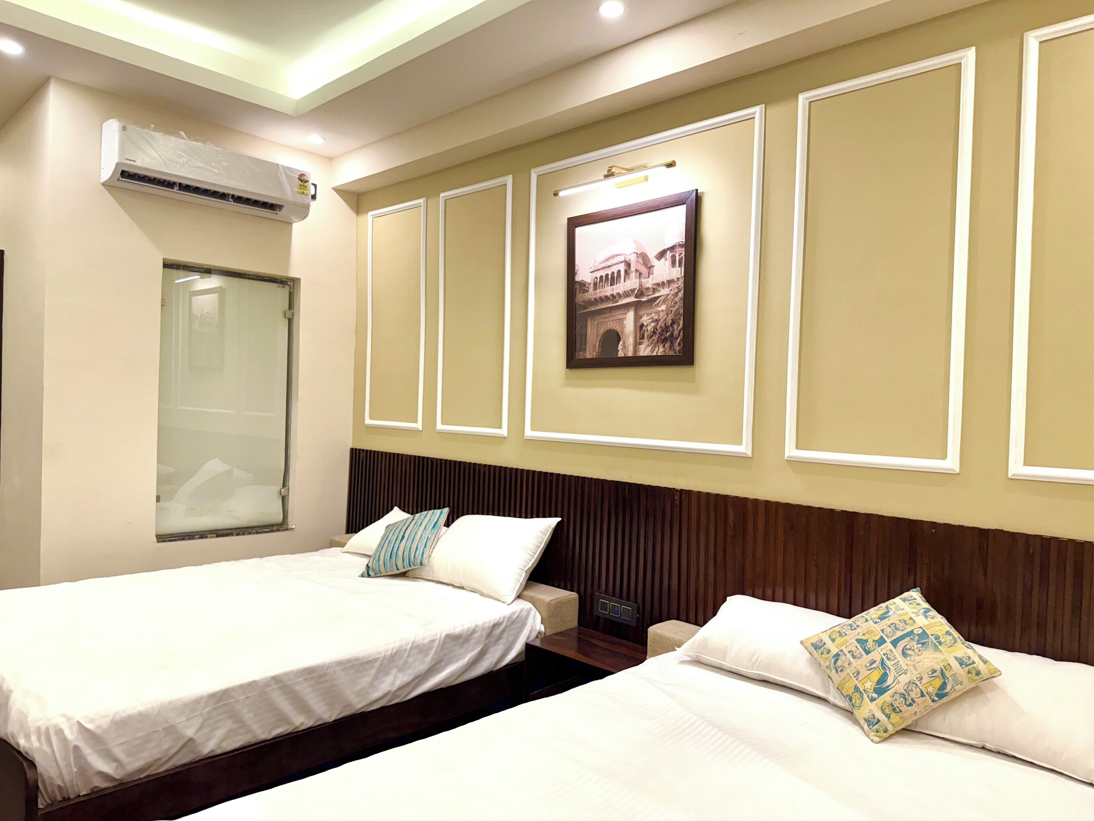 A hotel room with two beds, a large window, an air conditioning unit, and a framed picture on the wall.