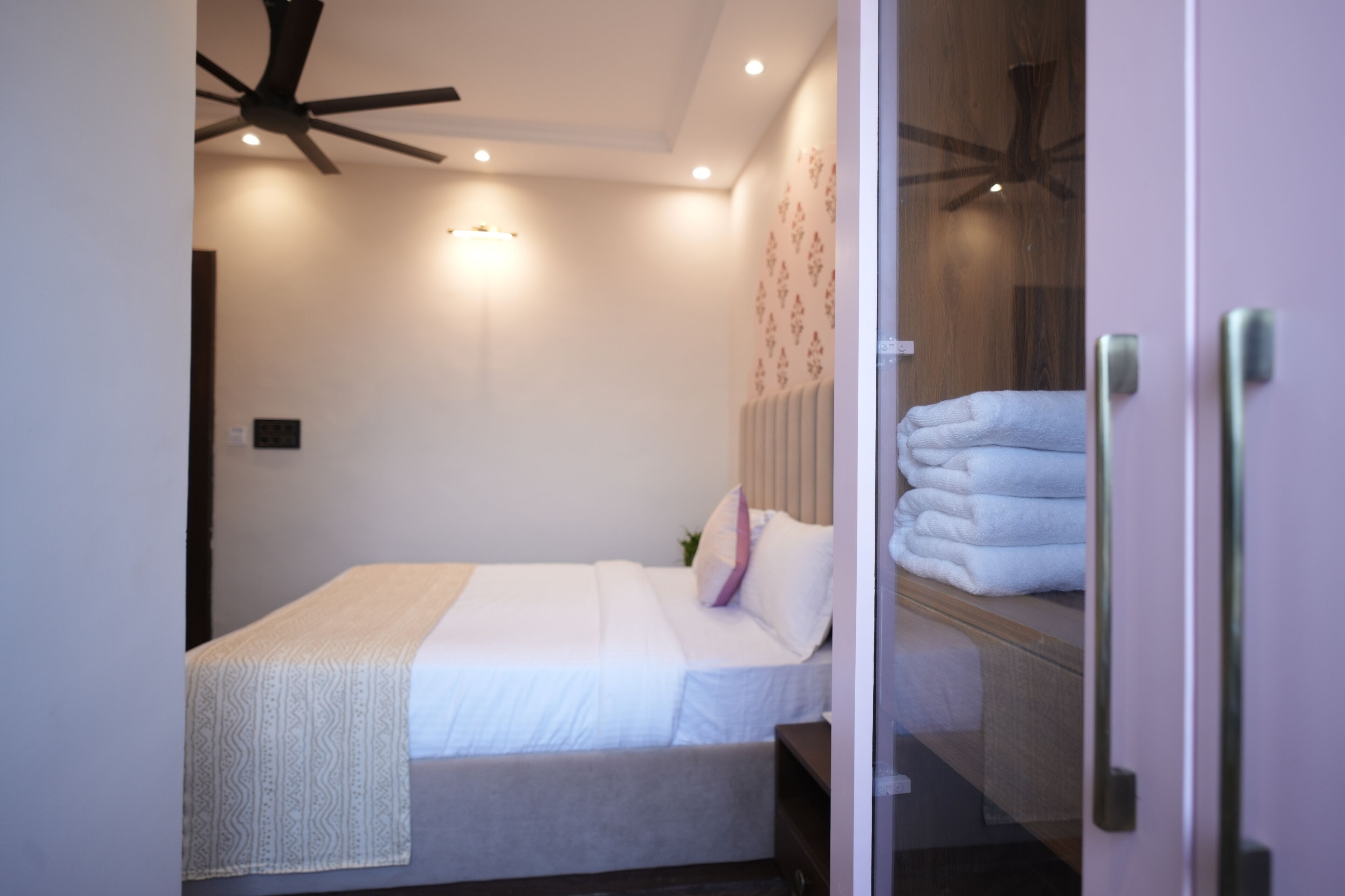 A neatly made bed with a white bedspread and pillows, a ceiling fan, and a wall-mounted light fixture.