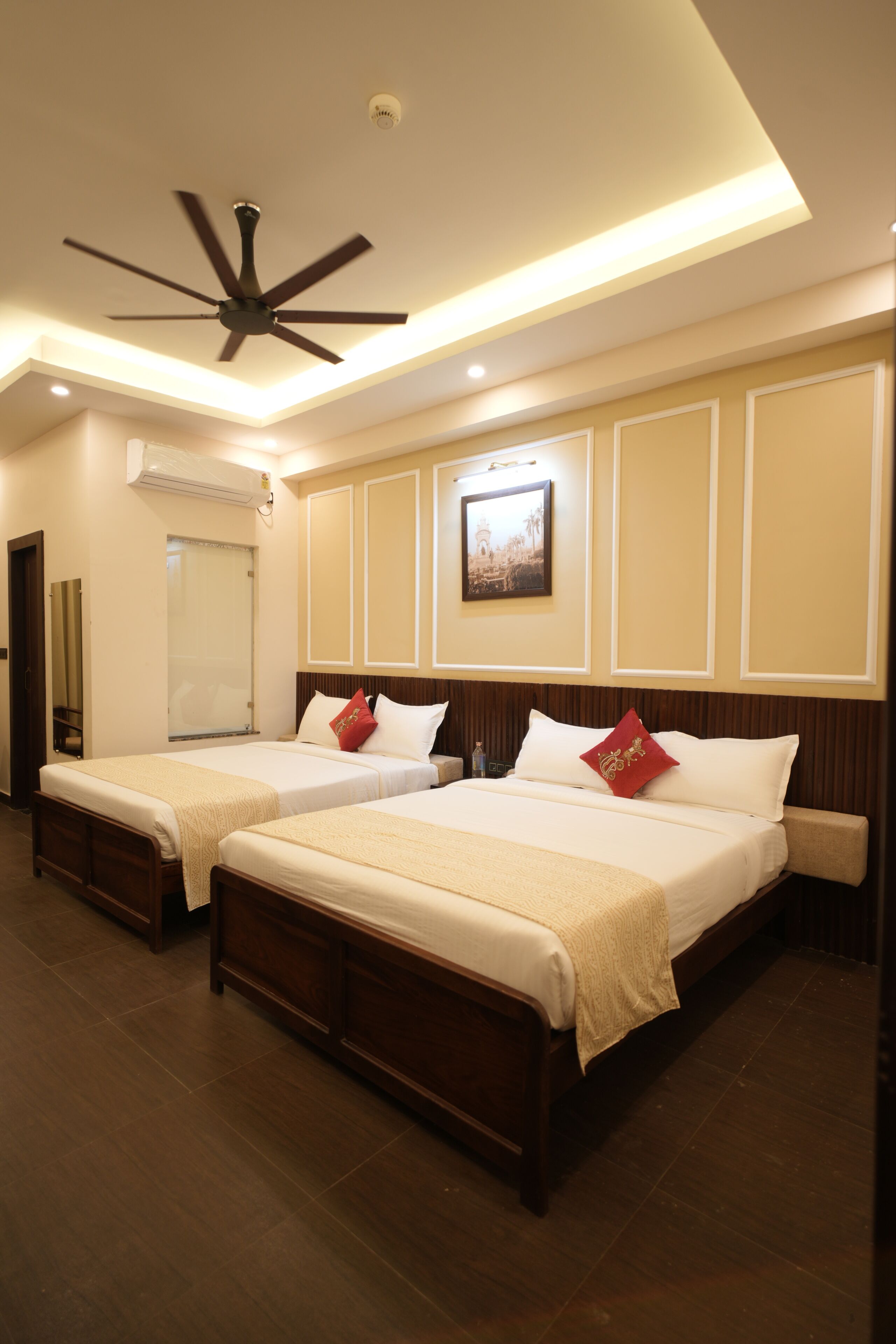 A hotel room with two beds, a ceiling fan, recessed lighting, a framed picture on the wall, and a wooden floor.