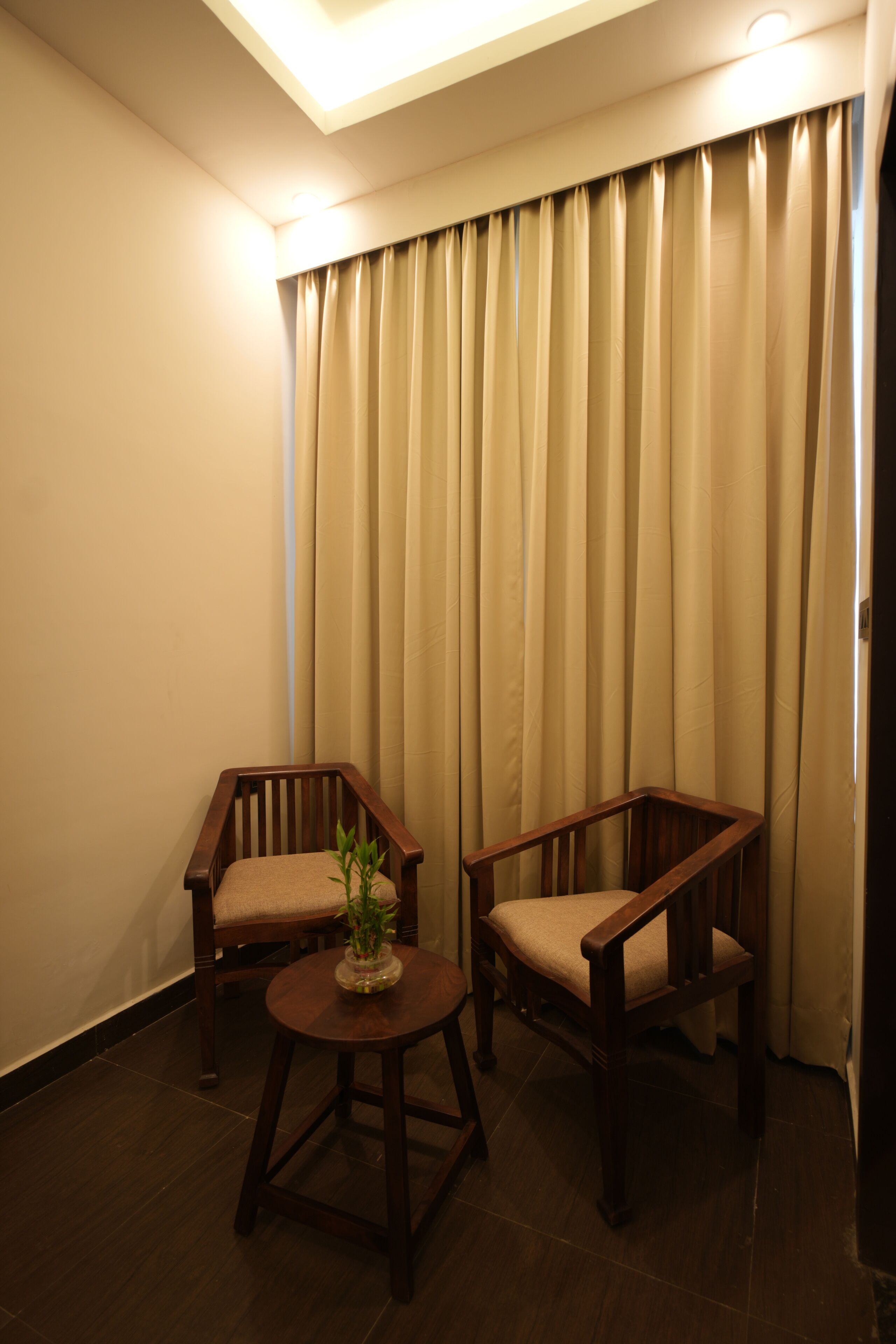 A room with two wooden chairs and a small round table, a potted plant, and beige curtains.