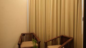 A room with two wooden chairs and a small round table, a potted plant, and beige curtains.