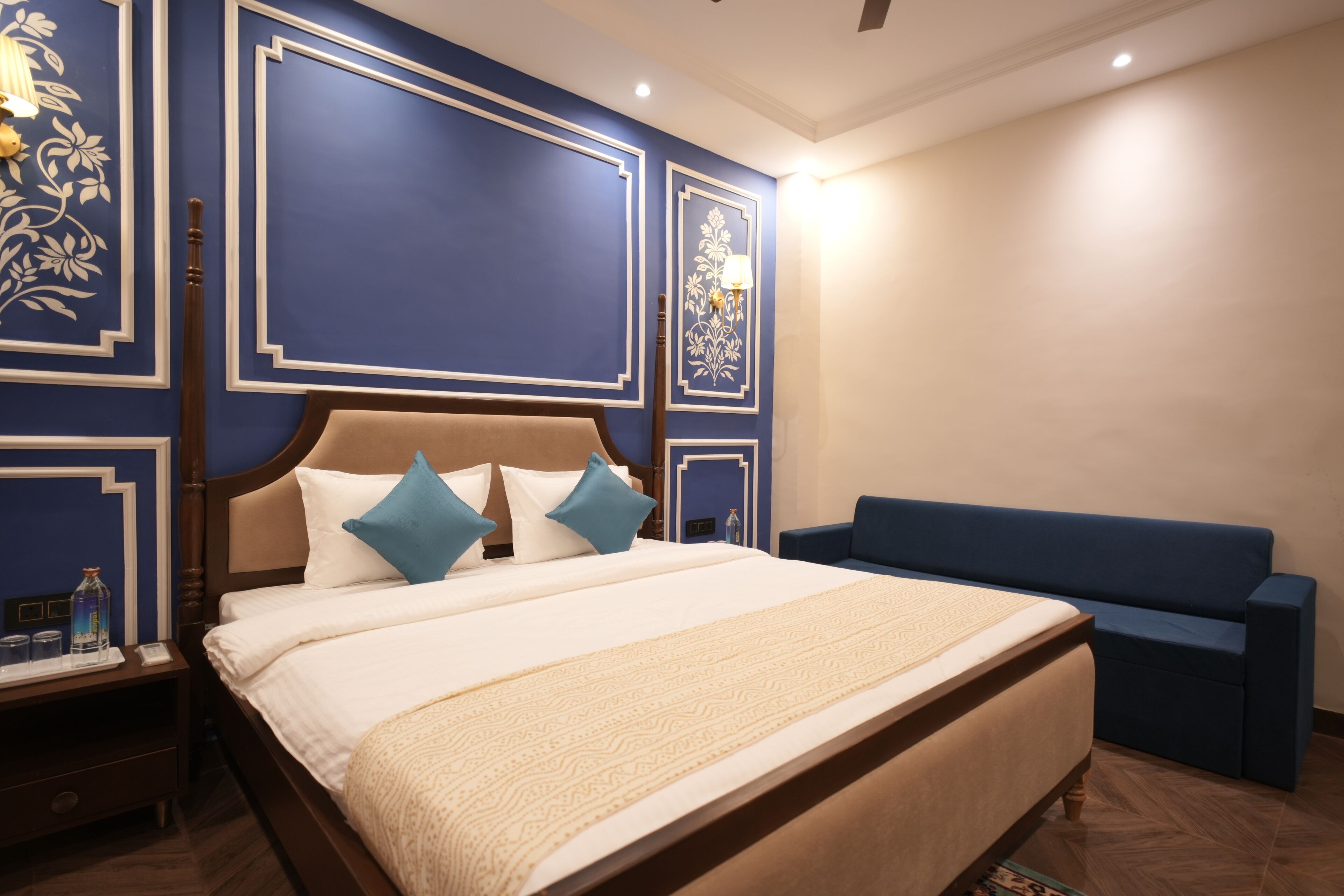 A neatly arranged bedroom with a large bed, a blue sofa, and decorative wall panels.