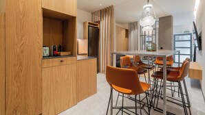 A modern kitchen with wooden cabinets, a stainless steel refrigerator, and a dining area with orange chairs and a glass table. - Dobo Madrid Goya (Madrid)