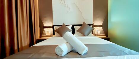 A neatly made bed with white linens and two rolled towels, a wall art piece, and two bedside lamps.