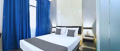 Quarto de hotel moderno com uma cama grande, cortinas azuis, parede de mármore e mesa de cabeceira com abajur.