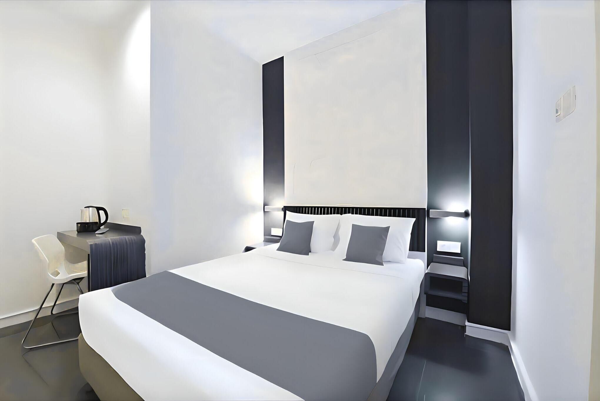A modern hotel room with a large bed, a desk with a chair, and a staircase.