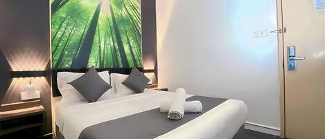 A hotel room with a large bed, a nightstand, a wall-mounted air conditioner, and a door.