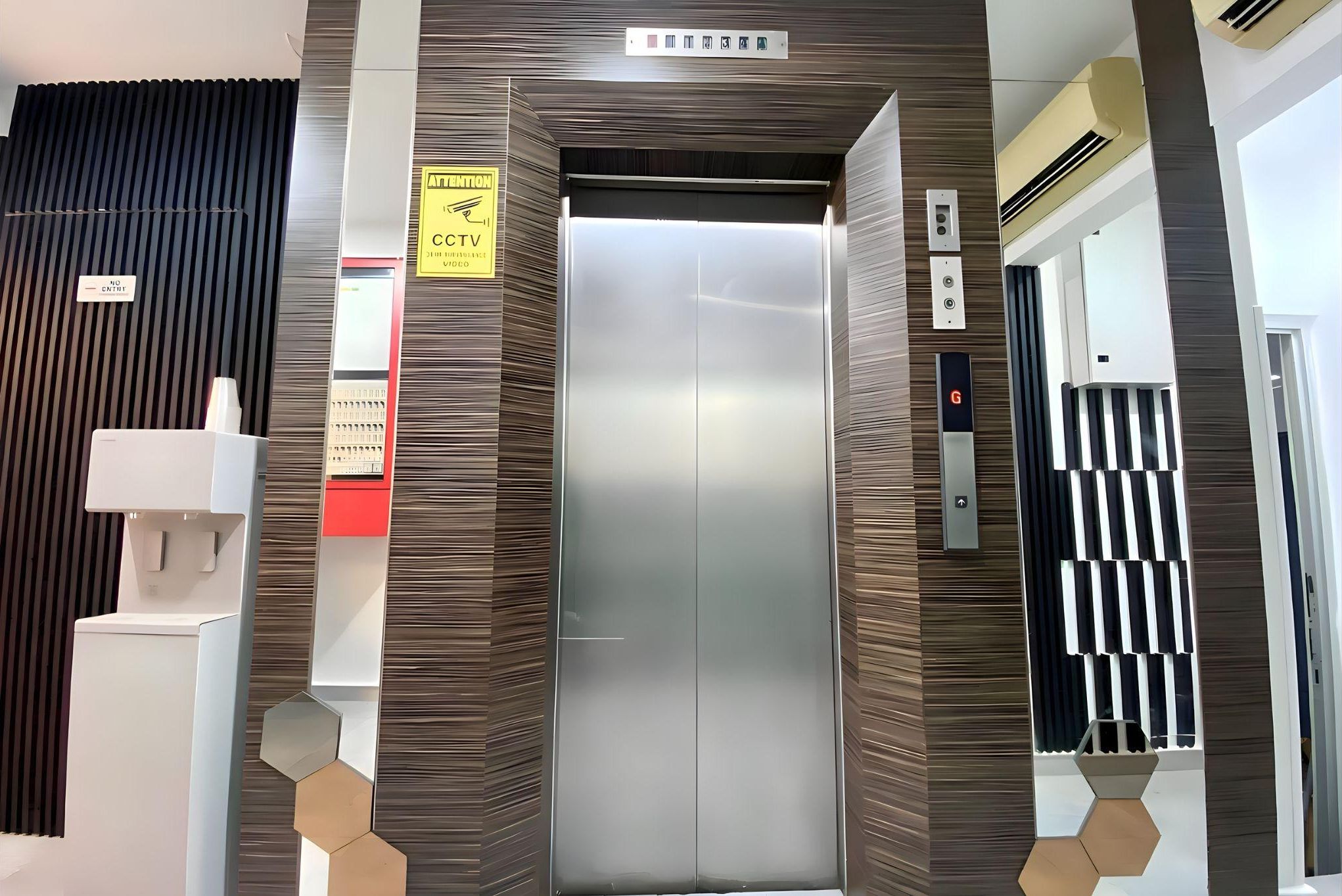 An elevator with a metallic finish, a caution sign, and a CTV security camera.