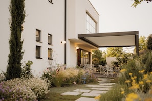 Una casa moderna con jardín, un patio con sillas y una zona exterior cubierta.