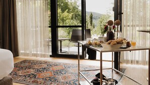 A room with a large window, a dining table with breakfast items, a patterned rug, and a chair. - Adults Only Boutique-Hotel maison 41 (Bad Gleichenberg)