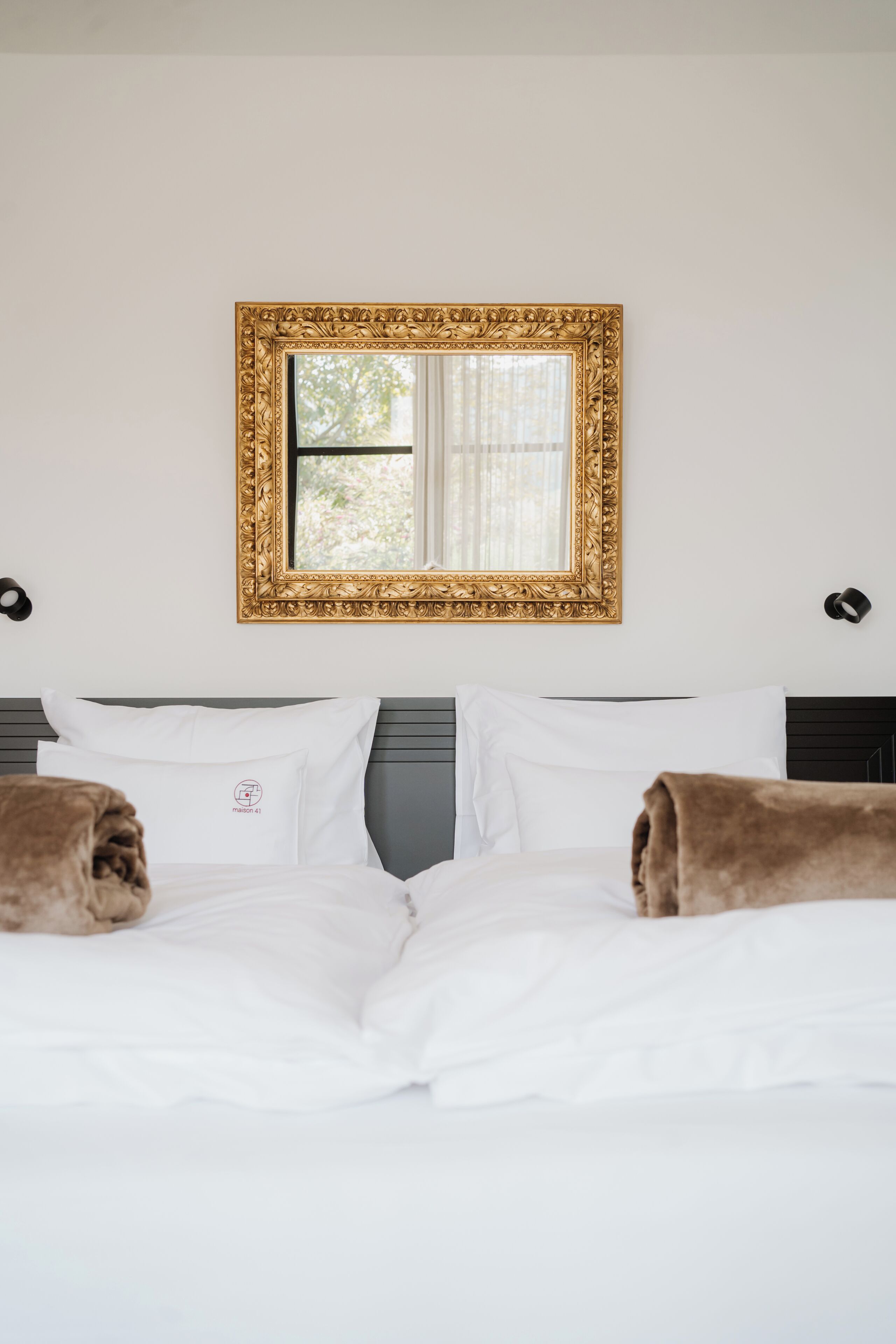 A hotel room with a large bed, white bedding, a gold-framed mirror, and two brown towels.