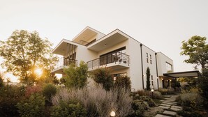 A modern two-story house with a balcony, surrounded by lush greenery and a stone pathway. - Adults Only Boutique-Hotel maison 41 (Bad Gleichenberg)