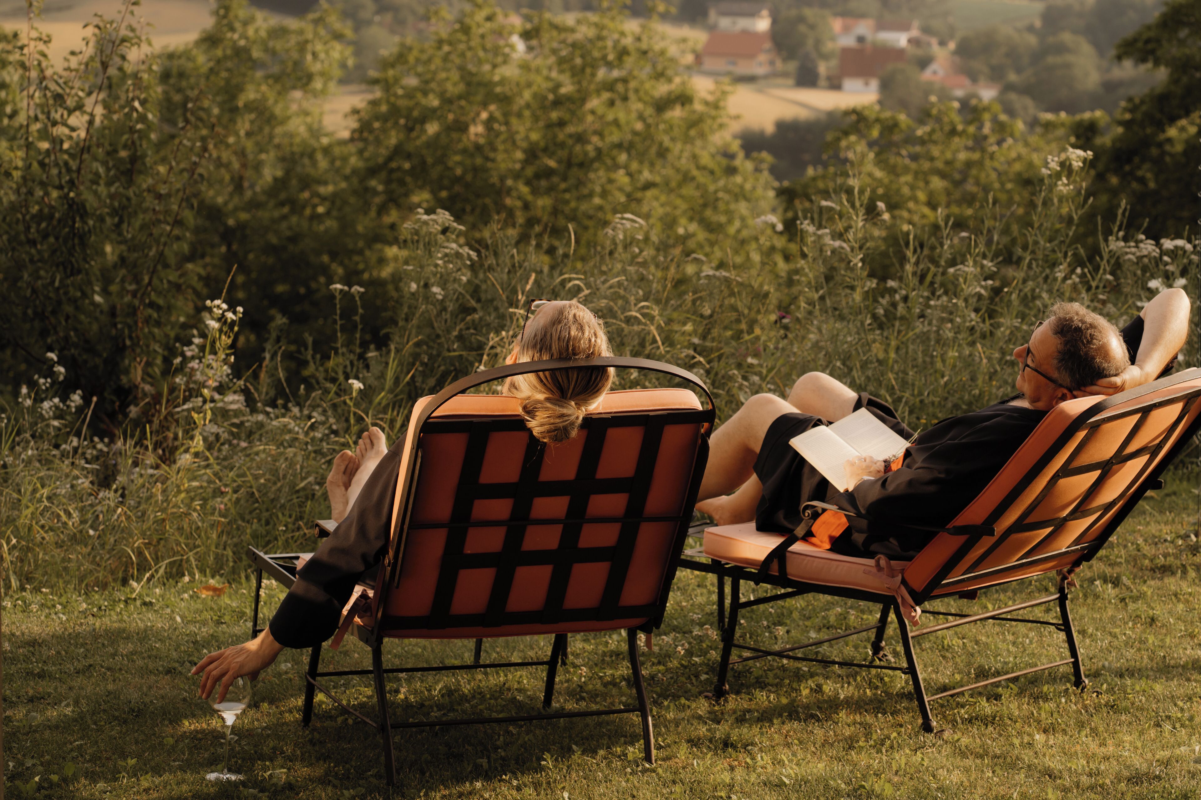 Two people sitting on a bench with a view of a grassy field and trees.