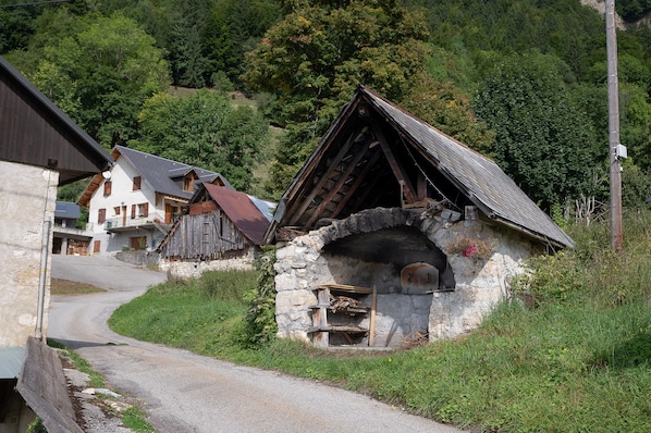 A rural road leading to a stone building with a wooden structure on top, surrounded by greenery and houses.