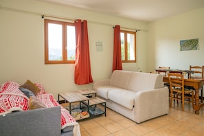 Un salon comprenant un canapé, une table basse, une table à manger avec des chaises et une fenêtre avec des rideaux.