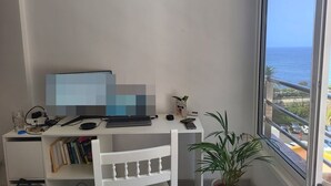 A room with a desk, computer, and a view of the sea.