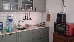 A kitchen with green cabinets, a sink, a countertop with various items, and a red microwave on a wooden cabinet.