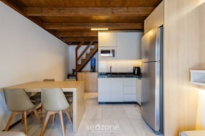 A compact kitchen with a built-in microwave, a stainless steel refrigerator, and a wooden dining table with chairs.