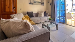 A modern living room with a grey sofa, a coffee table, and a large window with a view of a balcony.