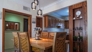 A dining area with a wooden table and chairs, a vase with flowers, and a clock on a wooden shelf.