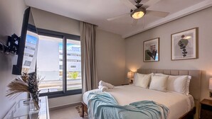 A hotel room with a bed, a desk, a ceiling fan, and a window with curtains. - Beautiful Brand new Beach Condo w Picuzzi (Punta Cana)