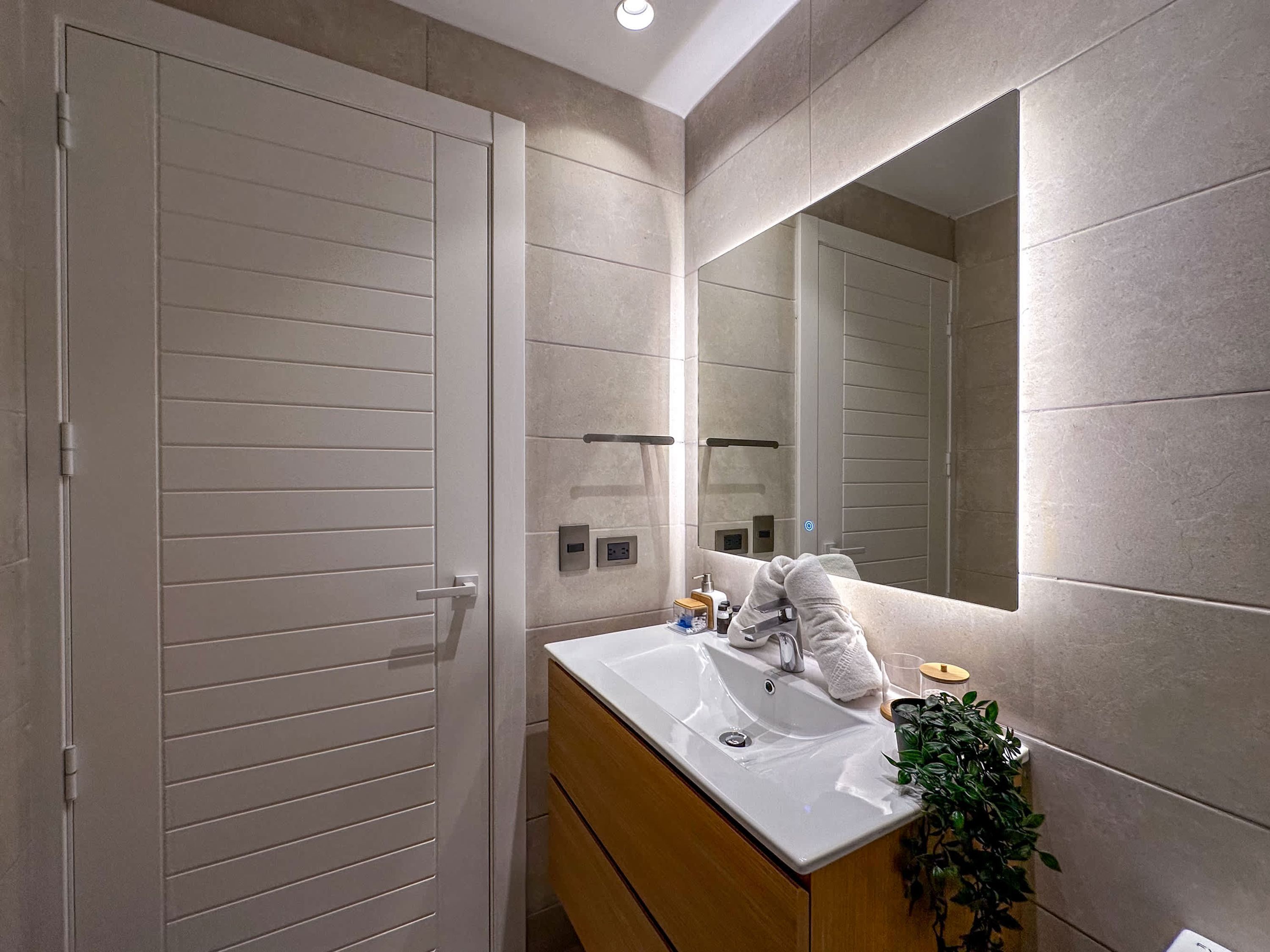 Un baño moderno con un espejo grande, un lavabo blanco y un mueble de tocador de madera.