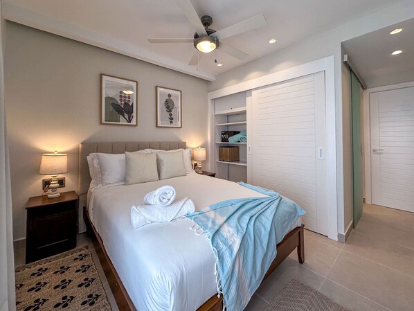 A neatly made bed with a blue blanket, a ceiling fan, and a bedside table with a lamp. - Beautiful Brand new Beach Condo w Picuzzi (Punta Cana)