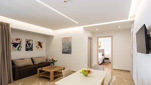 Una sala de estar moderna con sofá, mesa de centro y comedor, con un televisor montado en la pared.