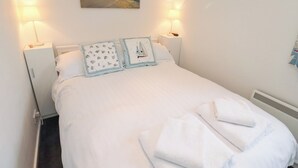 En pænt redt seng med hvide sengetæpper, to dekorative puder og et par hvide håndklæder.