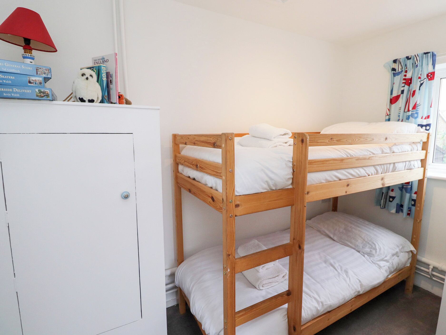 A bunk bed room with a white wardrobe, a red lamp, and a bookshelf with books and a stuffed toy.